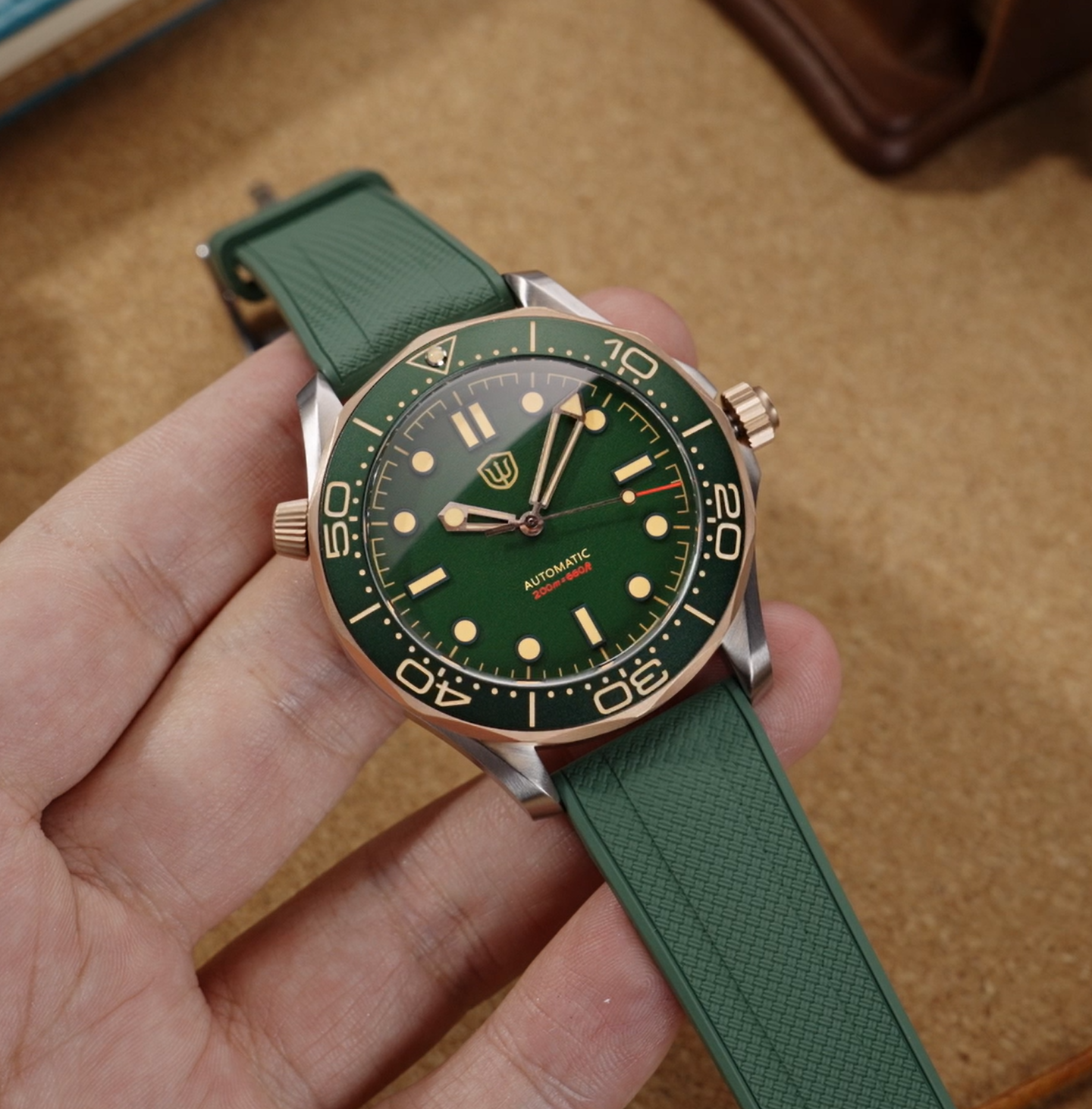 Hand-held green Watchdives WD007 with a bronze-tone bezel and textured green rubber strap